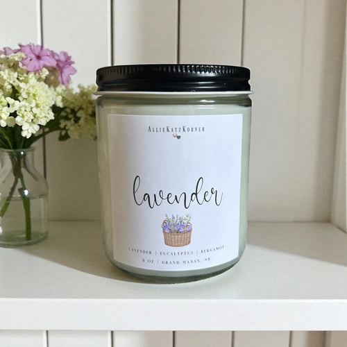 Lavender candle with a label on a white surface next to flowers